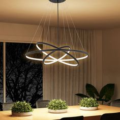 a modern chandelier hanging over a dining room table with potted plants on it