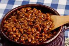 a wooden spoon in a red pot filled with baked beans on a checkered table cloth