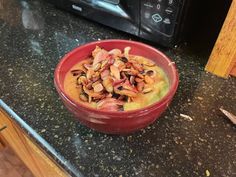 a red bowl filled with food sitting on top of a counter next to a microwave