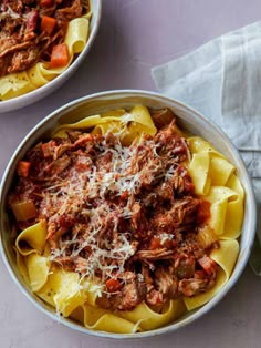 two bowls filled with pasta and meat on top of a white tablecloth next to napkins