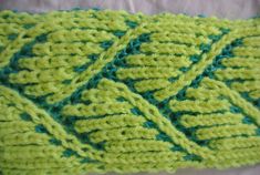 a knitted green and blue blanket sitting on top of a bed