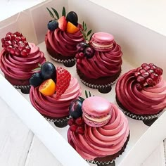 cupcakes with pink frosting and fruit toppings in a white cardboard box