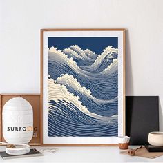 a blue and white wave art print on a shelf next to a vase with a cup