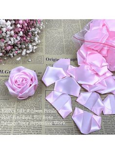 several pieces of pink satin ribbon sitting on top of a news paper next to flowers