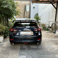 the back end of a black car parked in a garage next to trees and plants