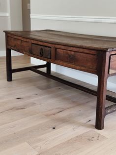 an old wooden table sitting on top of a hard wood floor next to a white wall