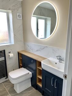 a white toilet sitting next to a bathroom sink under a round mirror on a wall