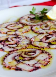 a white plate topped with sliced onions covered in sauce next to a lemon wedge on top of a red table cloth