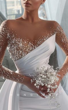 a woman in a white wedding dress with flowers on her shoulder and hands behind her back