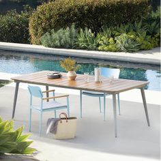 a wooden table sitting next to a pool in a backyard with chairs and a basket on it