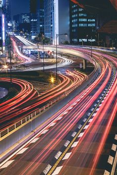 a city street filled with lots of traffic next to tall buildings at night, lit up by bright lights