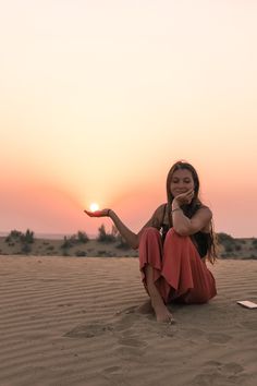 a woman is sitting in the sand with her hand out and smiling at the camera