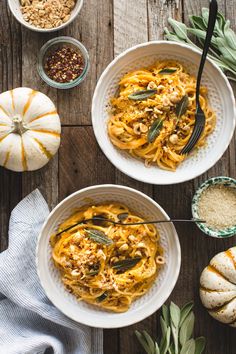 two white bowls filled with pasta on top of a wooden table next to pumpkins