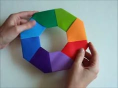 someone is holding a colorful origami piece in their left hand and the other hand is pointing at it