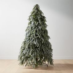 a small fir tree on a stand in front of a white wall and wooden floor