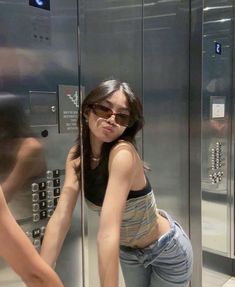 a woman standing in front of a metal elevator with her hand on the glass door