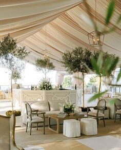 an outdoor event with tables and chairs under a tented area that has white drapes on the ceiling