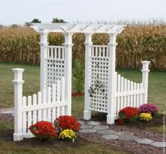 a white garden arbor with flowers in the foreground and corn behind it on a fall day