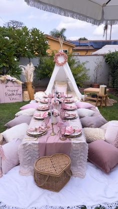 a table is set up with pink and white plates, napkins, and pillows