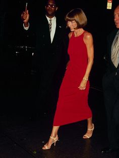 a woman in a red dress walking next to two men