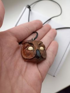 an owl necklace is being held in the palm of someone's hand with it's eyes open