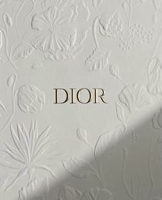 the word dior is written in gold on a white wall with floral designs and leaves