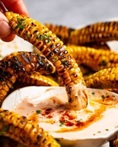 someone dipping some kind of sauce into corn on the cob with other food items