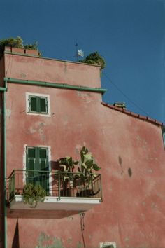 a pink building with green shutters and potted plants on the balconies