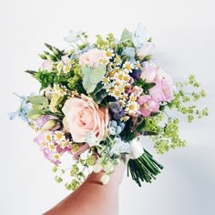 a woman's hand holding a bouquet of pink roses and blue forgeter daisies