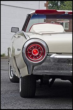 the rear end of an old car parked in front of a white building with red trim