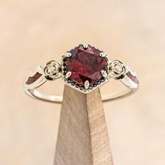 a close up of a ring on top of a wooden stand with a red stone