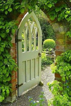 an open white door surrounded by greenery in a stone walled garden with gravel path