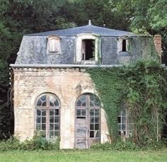 an old house with ivy growing on it's roof and windows in front of some trees