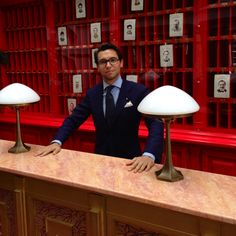 a man in a suit and tie standing behind a counter with two lamps on it