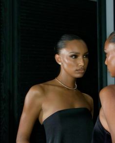 two women standing next to each other in front of a window wearing necklaces and dresses