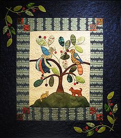 a quilted wall hanging with a tree and animals on it's side, surrounded by leaves