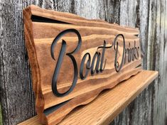 a wooden sign with the words boat dukes on it sitting on a bench in front of a wood fence