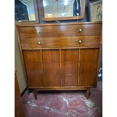 an old dresser with a mirror on top and other items in the back ground behind it