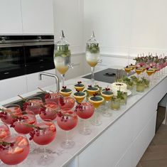 a long counter topped with lots of glasses filled with different types of drinks and garnishes