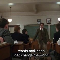 a group of people sitting at desks in front of a blackboard with words on it