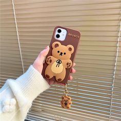 a person holding up a phone case with a teddy bear keychain attached to it