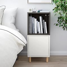 a white book shelf with books on it next to a bed and potted plant