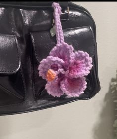 a crocheted flower hanging from the side of a black leather handbag on a hook