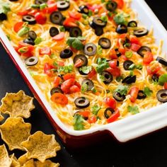 an enchilada casserole in a red dish with black olives and tomatoes