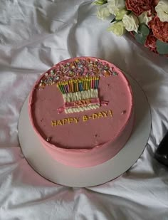 a pink birthday cake sitting on top of a table next to a vase with flowers