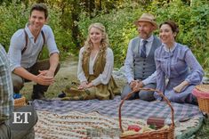 four people are sitting on a blanket in the woods, smiling and having picnic time