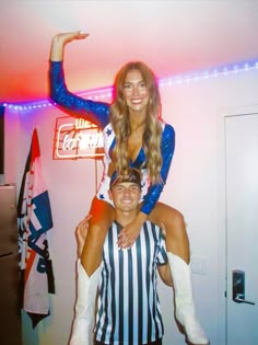 a woman is sitting on the back of a man in a referee outfit and holding his arm up