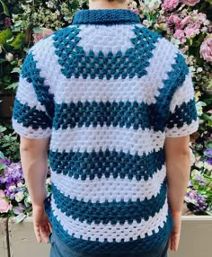 a man wearing a blue and white crocheted sweater standing in front of flowers