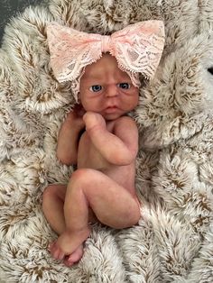 a baby doll with a pink bow on it's head sitting in a pile of fur