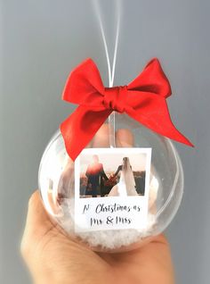 a hand holding a glass ornament with a red bow on it and a photo inside